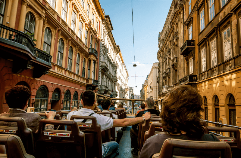 Point of view from a seat on a roofless bus with buildings on the sides