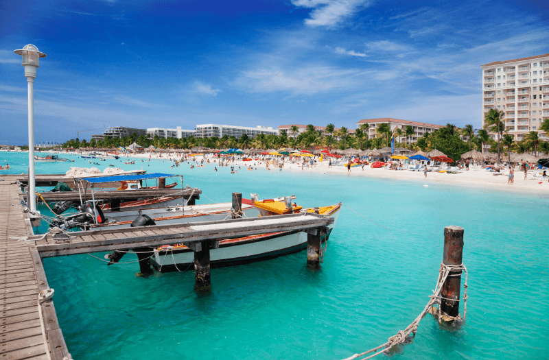 Beachfront dock with boats tied up, with buildings and clear sky in the background