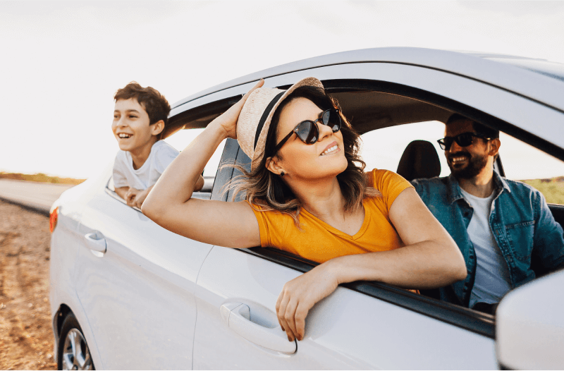 Woman wearing hat and child, leaning out of car windows, and man in driver's seat