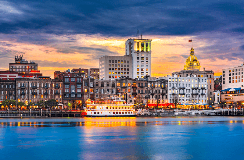 View of a river bank with buildings and a ferry, with the sunset sky in the background