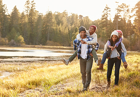 A Black family walking near a river in a wooded area